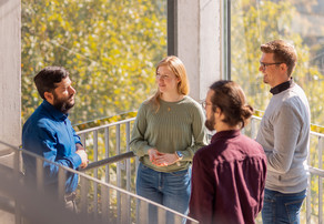 Gespräch im Treppenhaus Vier Personen stehen vor einem Fenster im Treppenhaus eines Universitätsgebäudes und unterhalten sich.